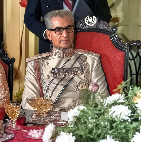 His Majesty, the Shah of Iran in an ornate light-colored military uniform sits in a red velvet chair behind a table — a public domain photograph from The Shah of Iran archive documenting the Pahlavi era.