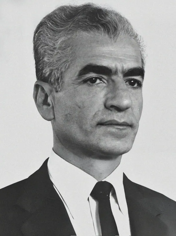 His Majesty, the Shah of Iran with graying hair wears a dark suit, white shirt, and dark tie in a portrait — a public domain photograph from The Shah of Iran archive documenting the Pahlavi era.
